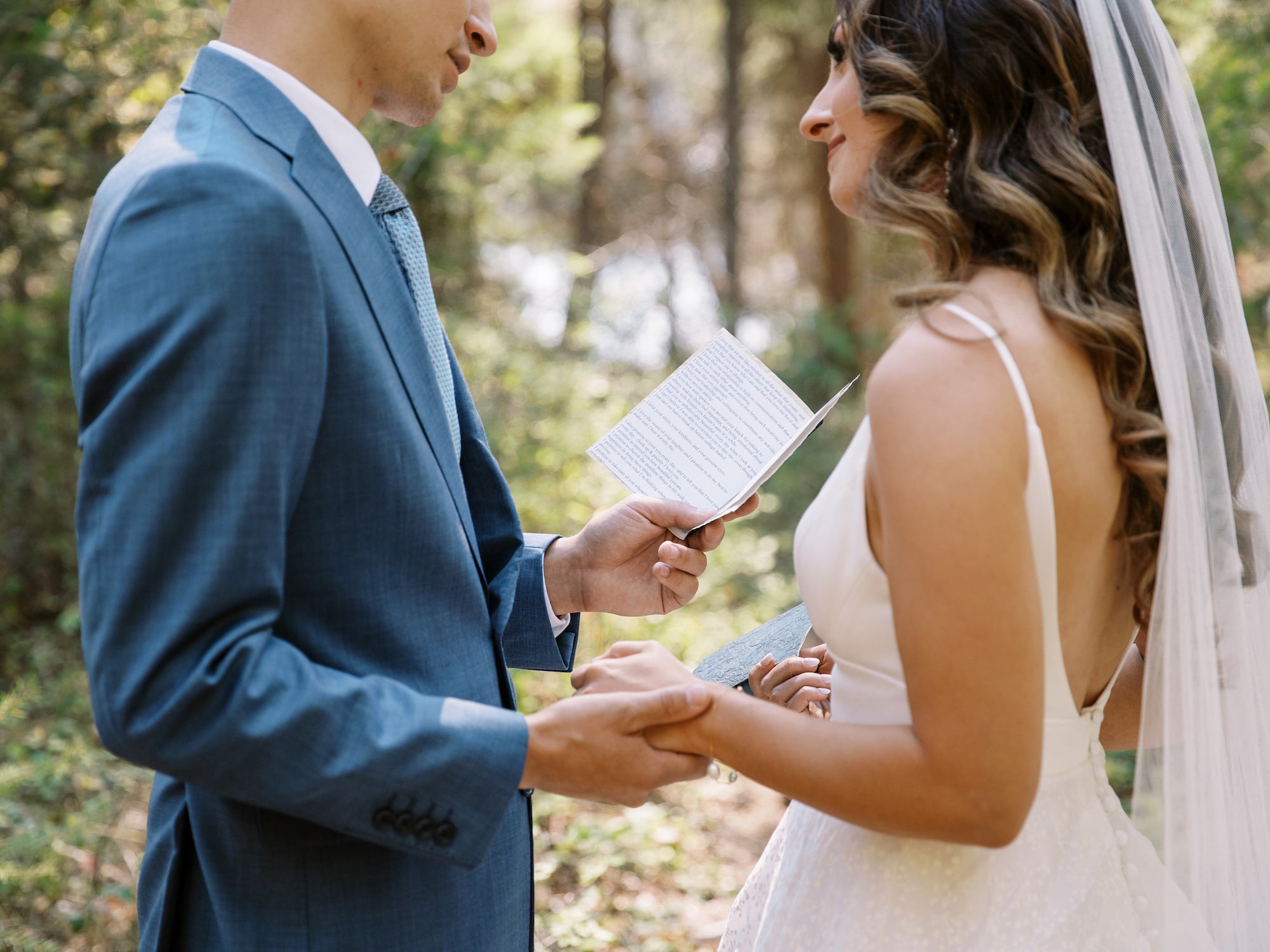 Jeune homme lisant ses voeux à sa future femme dans des tenues de mariage en plein air