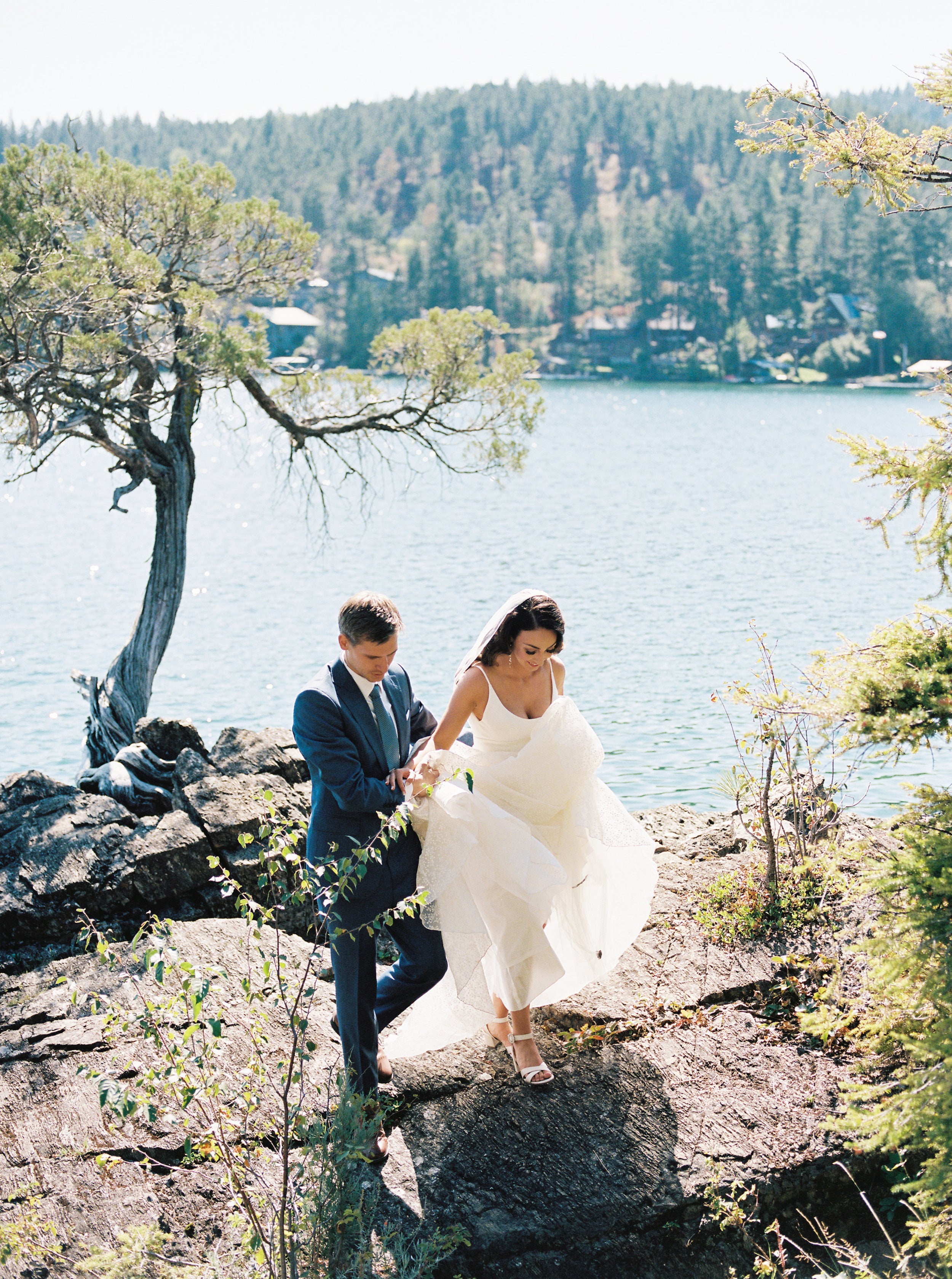 Femme qui monte sur un rocher avec sa robe de mariée et ces accessoires avec l'aide de son mari