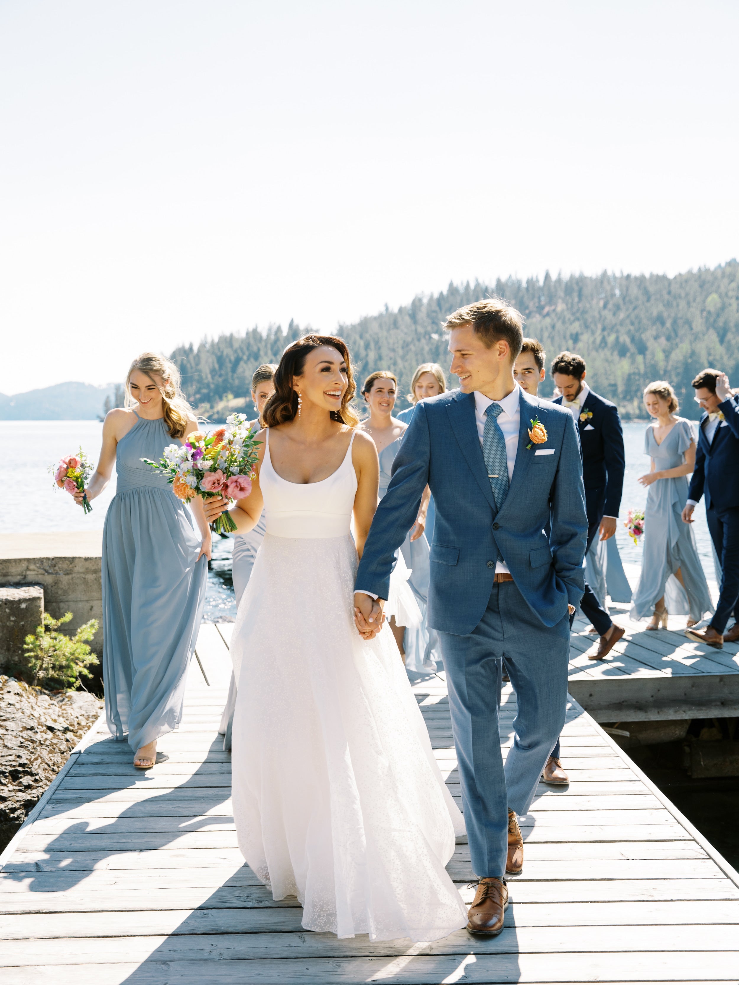 Couple de jeune mariés marchant en souriant avec les demoiselles et garçons d'honneurs qui les suivent