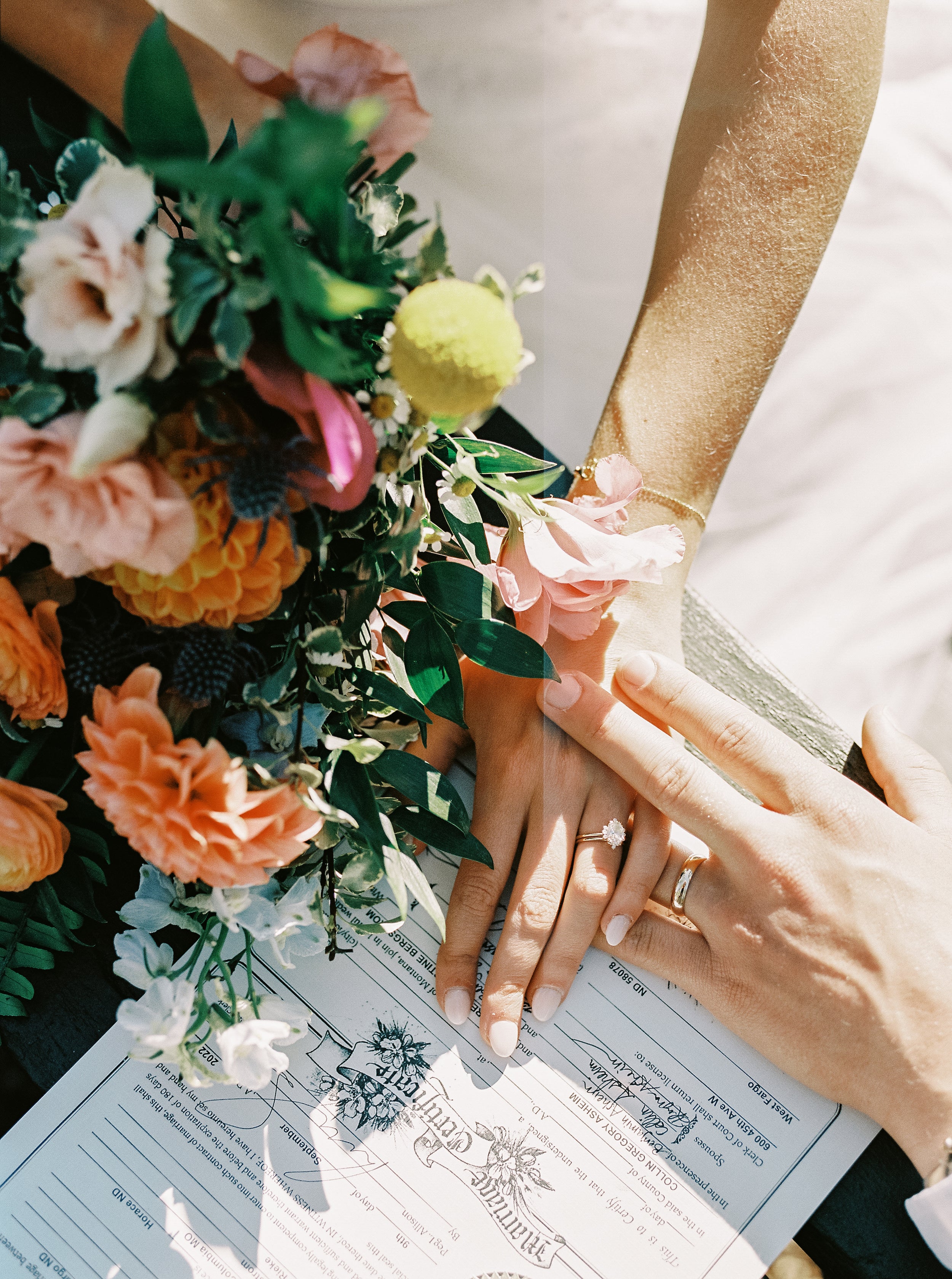 Plan sur les mains des mariés montrant les bijoux de mariage notamment la bague et le bracelet ainsi que le bouquet