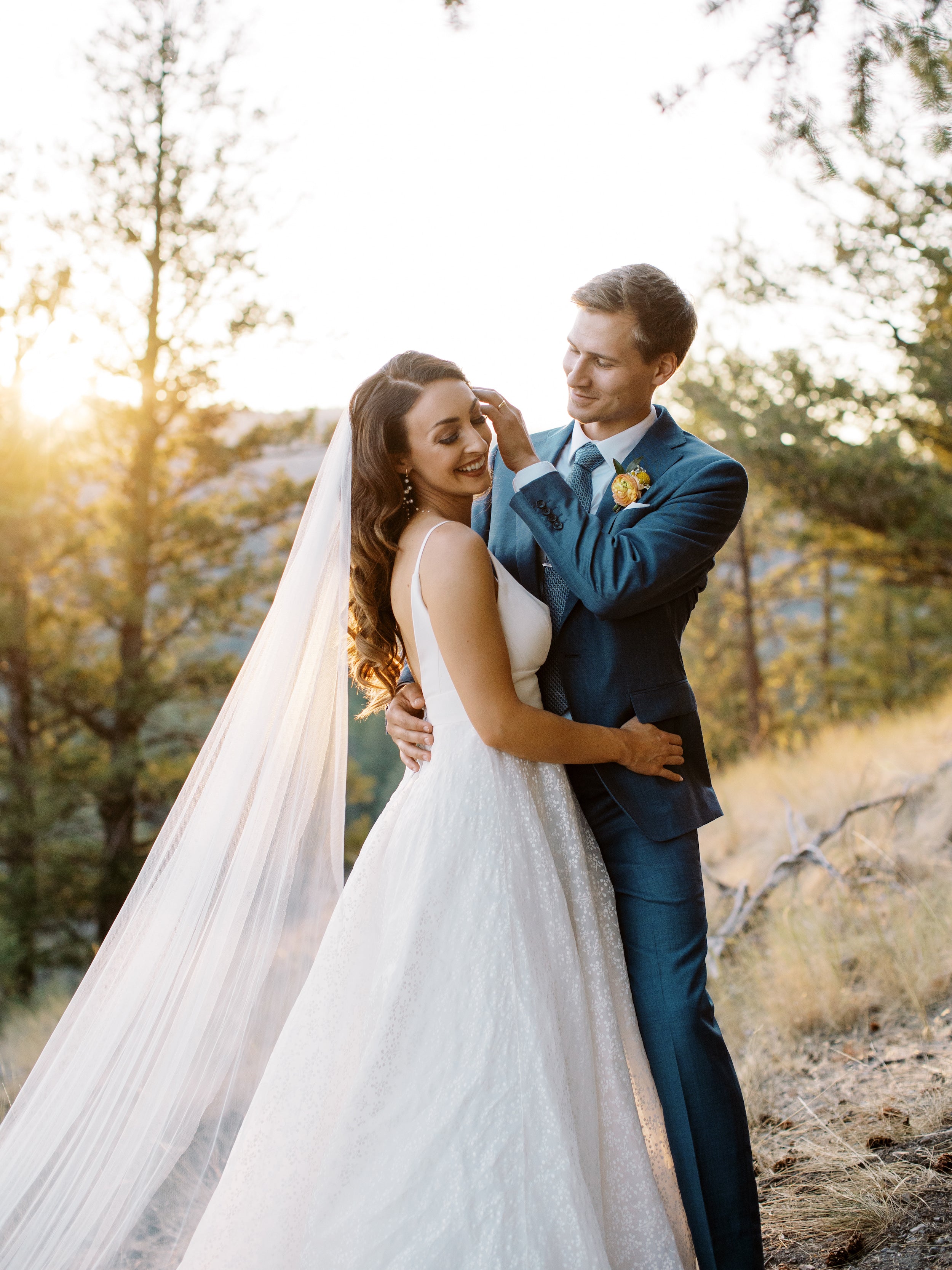 Le marié qui remet en place une mèche de cheveux de la mariée dans sa robe blanche son voile et ces accessoires mariage