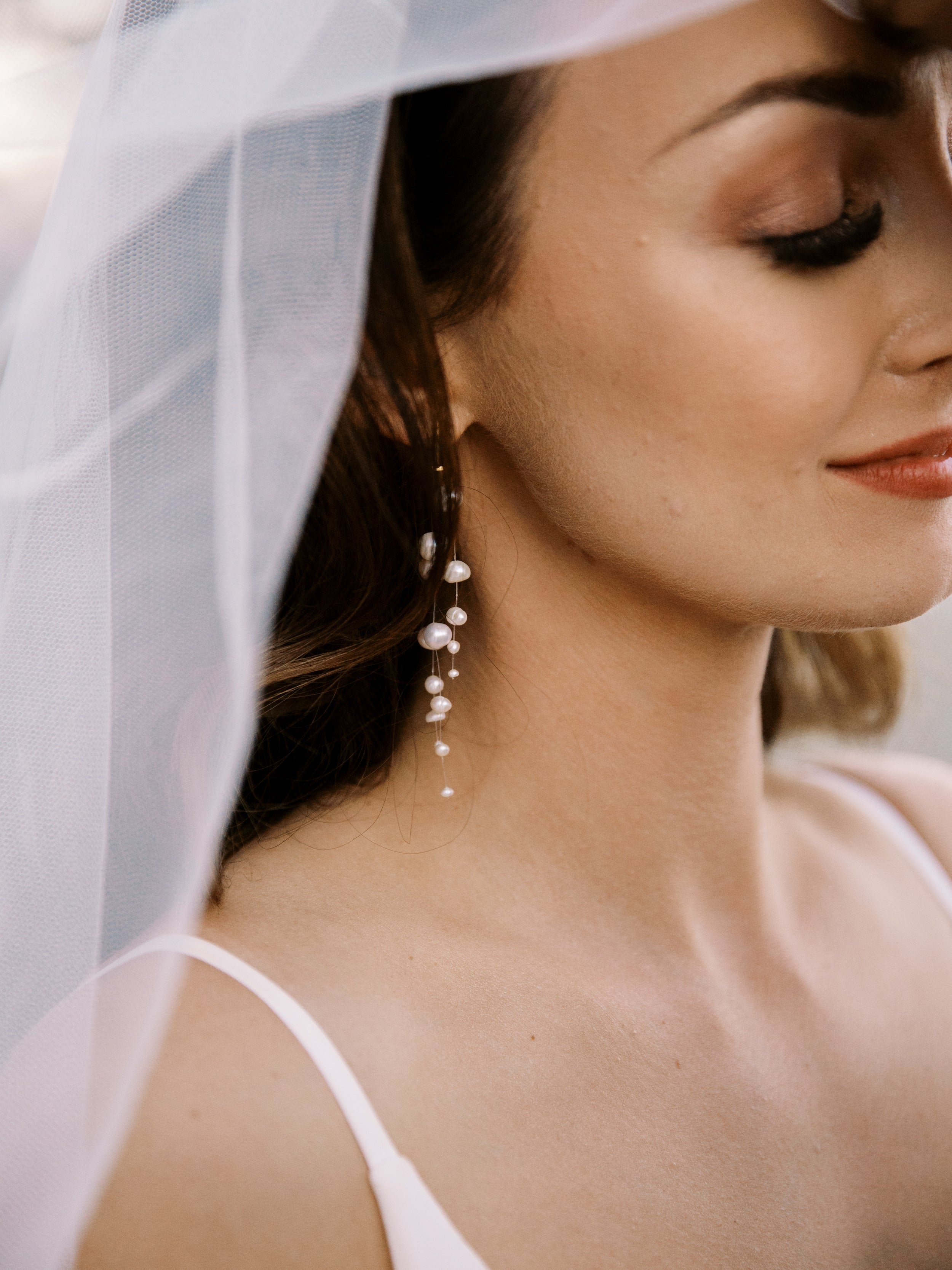 Focus sur le profil d'une femme portant des boucles d'oreilles de mariage en perles naturelles asymétrique