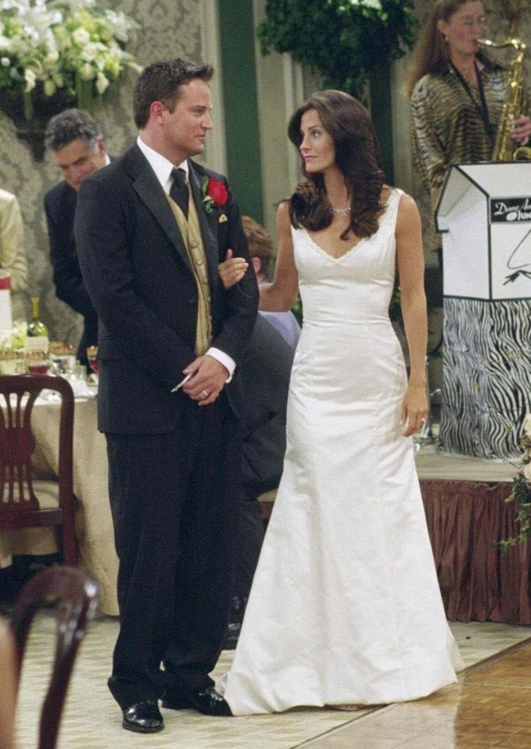 Monica dans une robe blanche de mariage luxe tenant le bras de Chandler