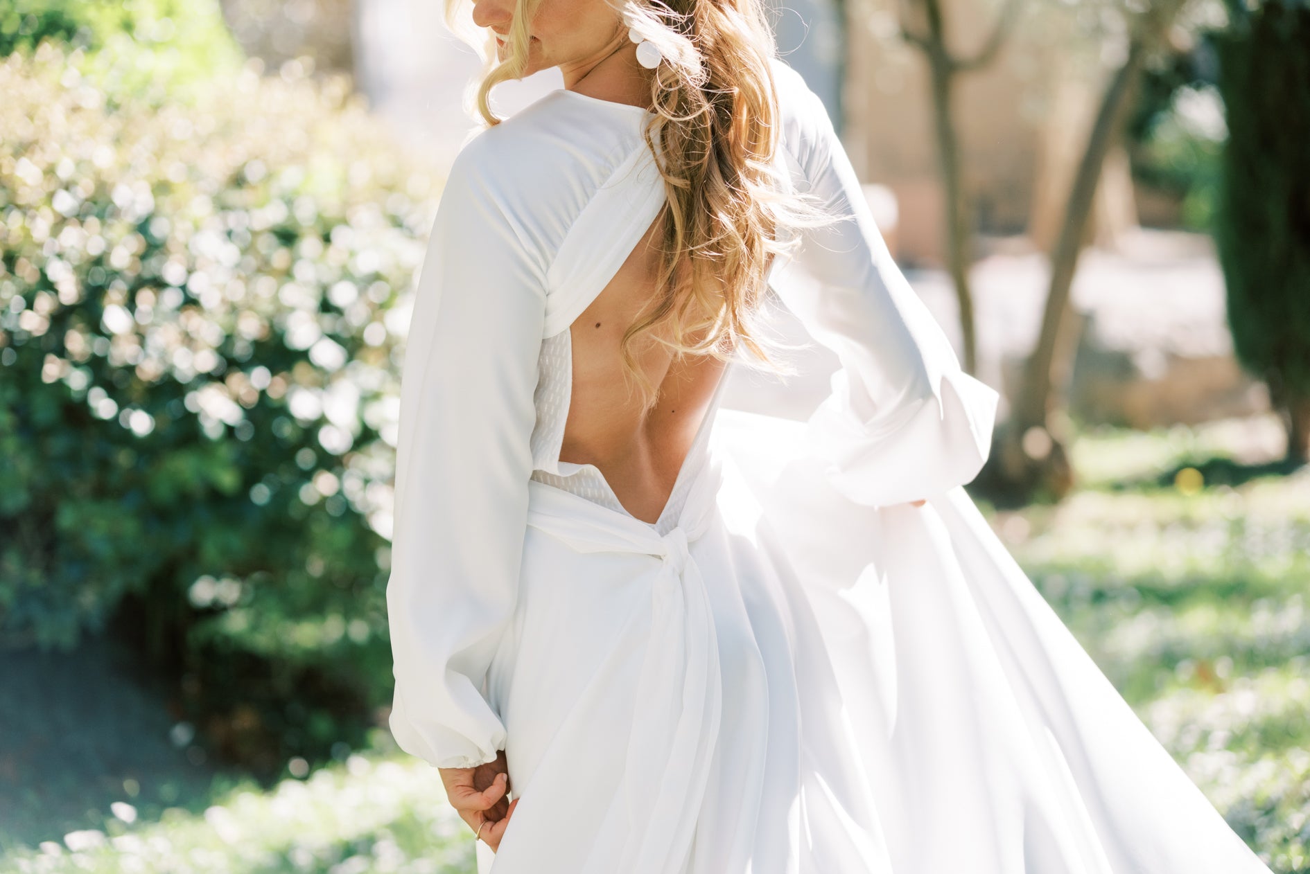 Femme de de dos dans sa robe de mariée avec un décolleté de dos et des manches longues