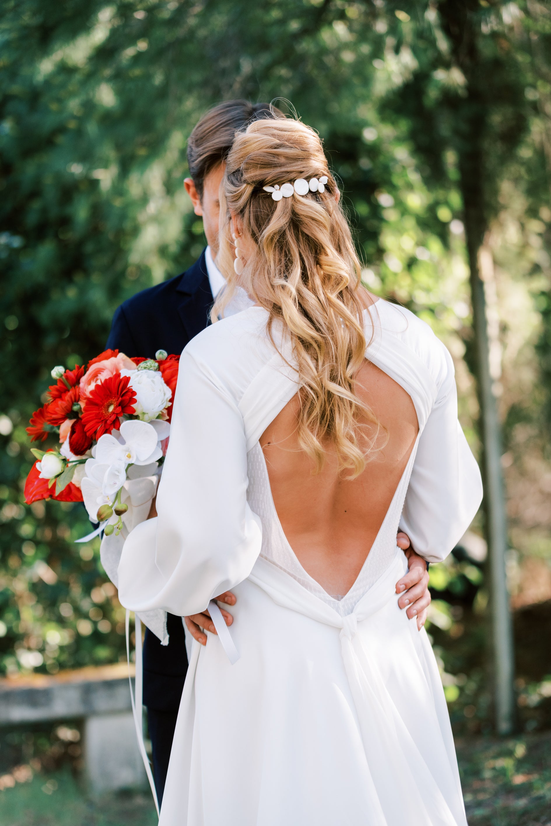 Femme de dos dansant avec son mari en portant un bouquet de fleur et sa robe de mariée mettant en valeur sa coiffure avec son accessoire de cheveux mariage en nacre