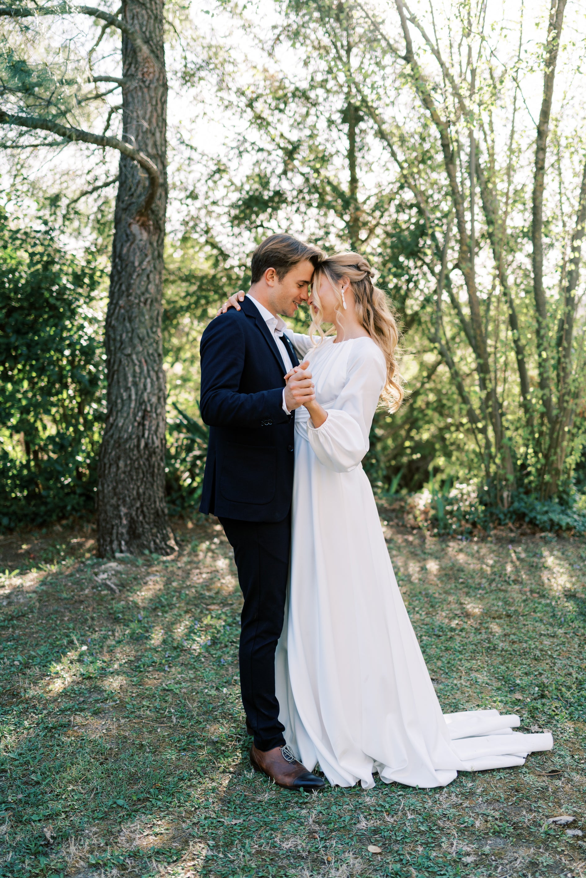 Deux mariés qui dansent en extérieur front contre front dans leurs tenues de mariage portant des accessoires pour les mariés