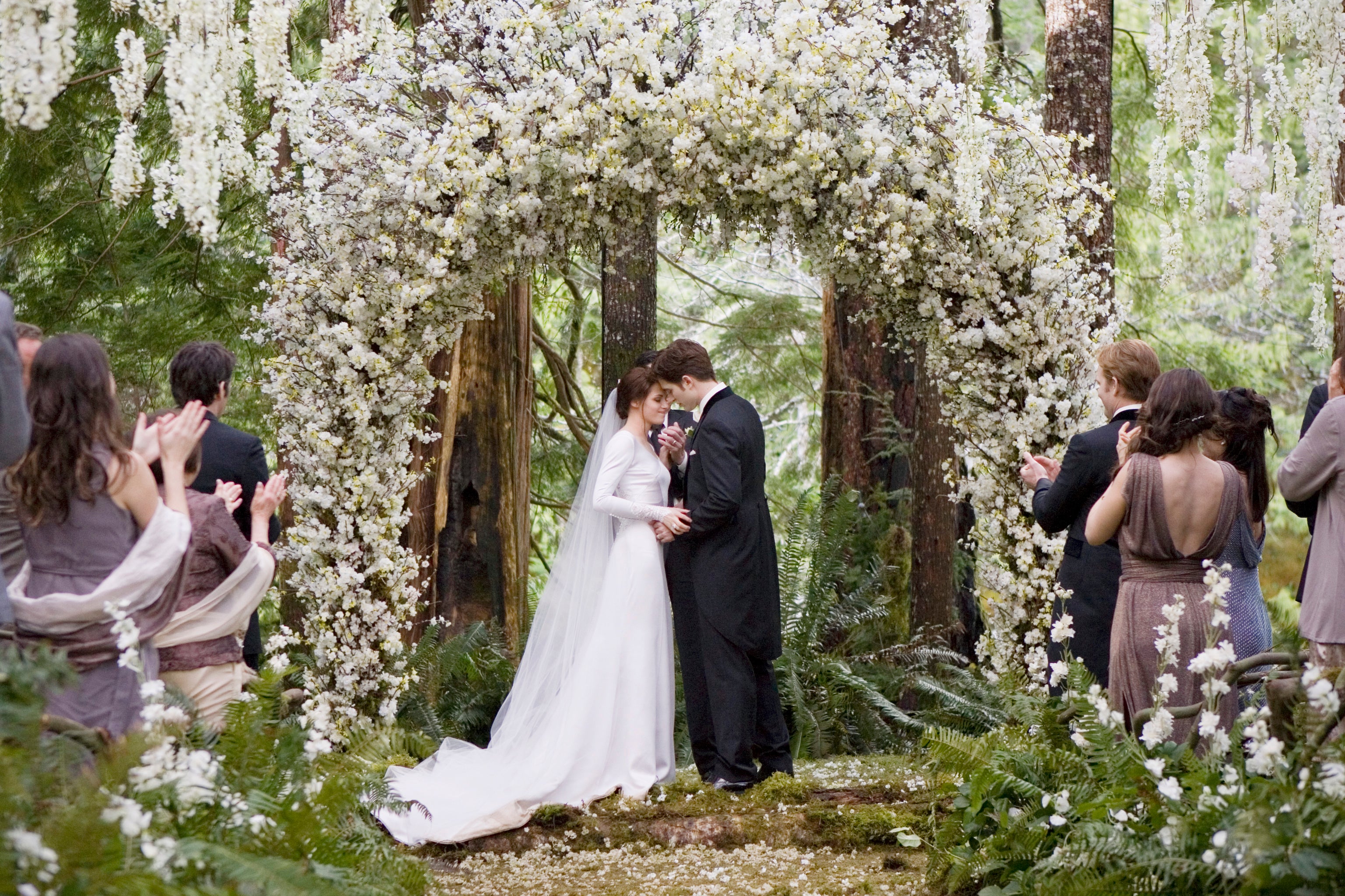 Bella dans sa robe blanche minimaliste se mariant avec Edward sous une arche de fleur 