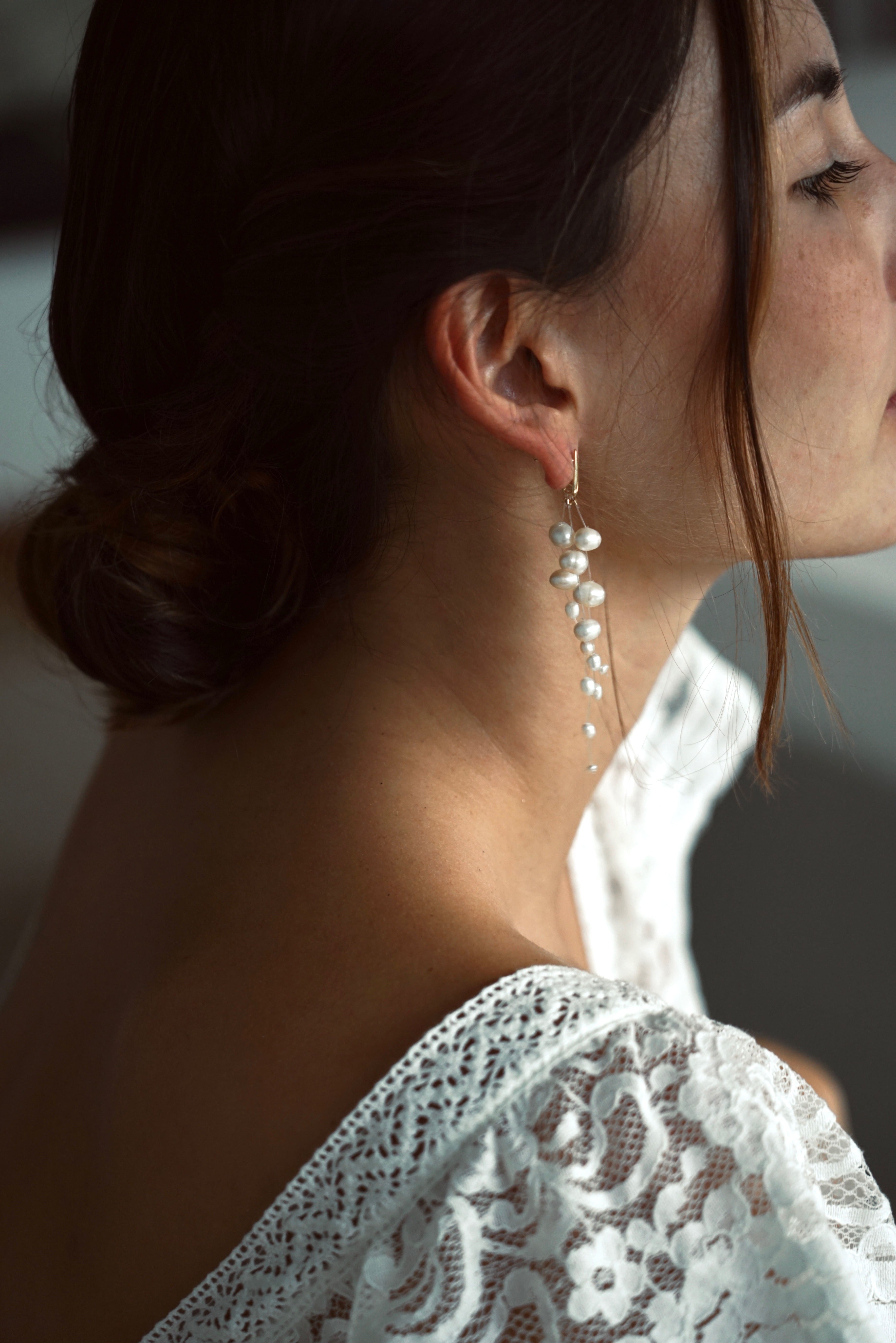 Mariée portant des boucles d'oreilles pendantes bohèmes et élégantes fait de trois fils transparents auxquels sont enfilées de belles perles naturelles blanches